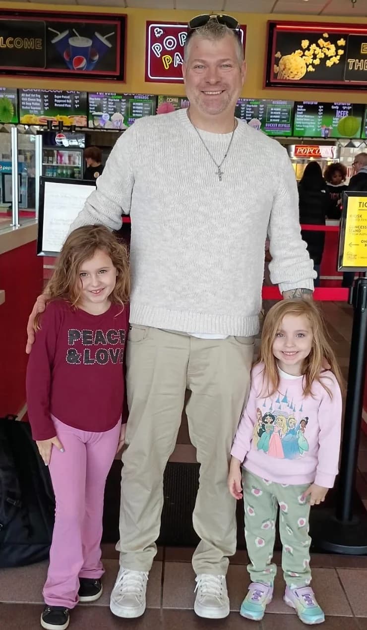 Jerry Ondo, smiling, standing tall between two young girls.